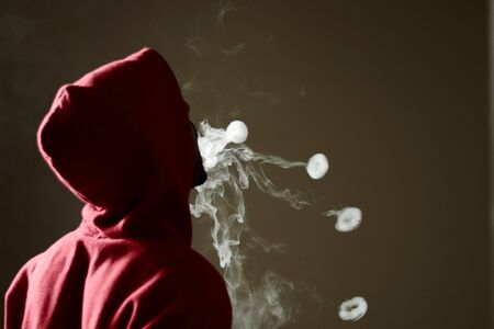 Young male in red hoodie vaping smoking, blows 4 smoke rings, isolated rear viewの写真素材