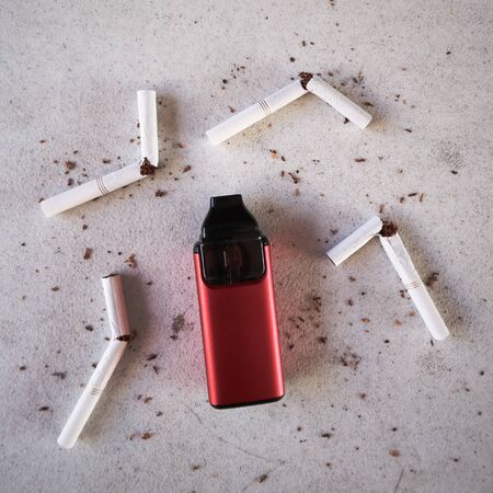 Single red vape electronic cigarette as smoking alternative with broken cigarettes and scattered tobacco on white textured background isolatedの写真素材