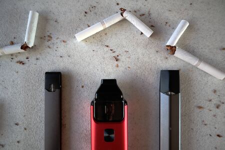 Different vape devices electronic cigarettes as smoking alternatives with broken cigarettes and scattered tobacco on white textured background close upの写真素材