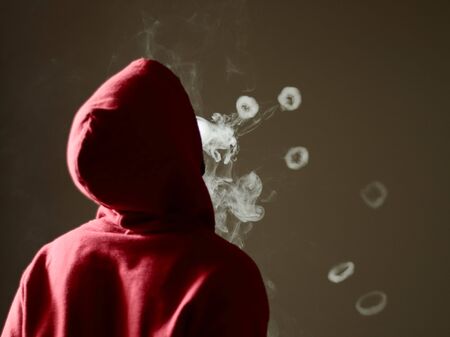 Young male in red hoodie vaping smoking, blows many smoke rings, isolated rear viewの写真素材
