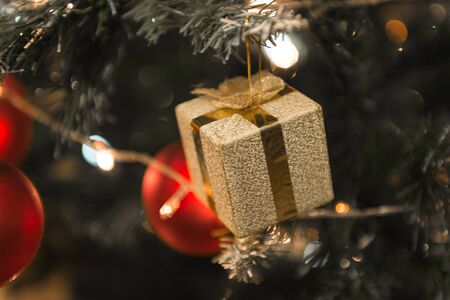 Christmas golden present hanging on a beautiful Chrismas tree surrounded by red shinning ballの写真素材