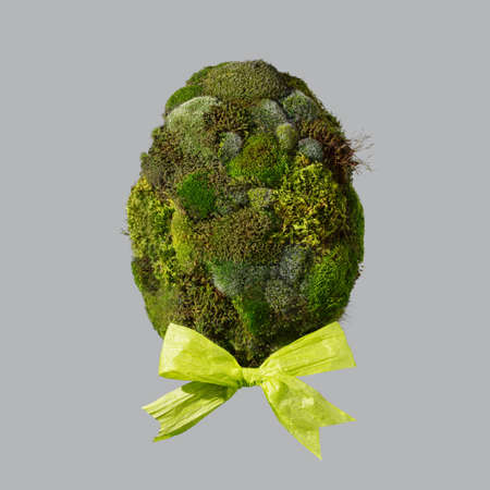 Easter egg shape made of fresh spring moss and pastel yellow paper bow on light grey background. Minimal Easter holiday concept.の写真素材