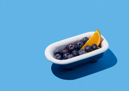 Fresh slice of fruit and blueberries in bathtub on pastel blue background. Creative minimal summer idea.の写真素材
