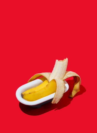Fresh banana fruit in bathtub on bright red background. Minimal summer concept.の写真素材