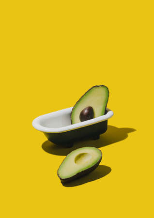 Fresh and ripe slices of avocado fruit in bathtub on pastel yellow background. Creative minimal summer idea.の写真素材