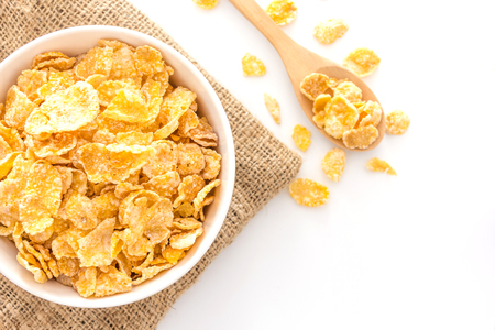 bowl of cornflakes and cornflakes on wooden spoon over a sackcloth on white table background, Top...