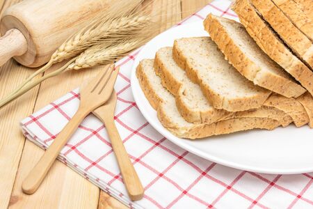 Sliced wholemeal bread on white plate with wheat ears on wooden table background, Closed up