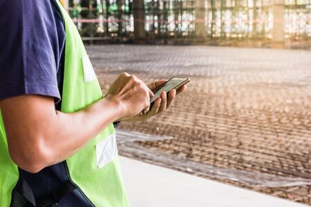 Construction worker with green helmet working on construction site using smartphone, selective focusの写真素材