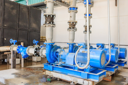 Large industrial water treatment and boiler room. Shiny steel metal pipes and blue pumps and valves.