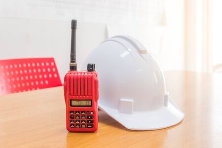 Red walkie-talkie radio and a white safety helmet on wooden backgroundの写真素材