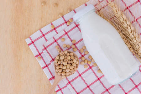 soy milk in glass bottle with soy beans in spoon on wooden background, Top view with copy space and text.の写真素材