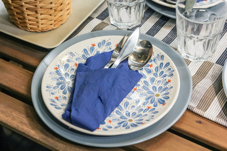 Cutlery set with indigo linen napkin in white plate on a wooden table in a restaurant table setting,...