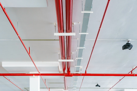 Fire sprinkler system with red pipes is placed to hanging from the ceiling inside of an unfinished...