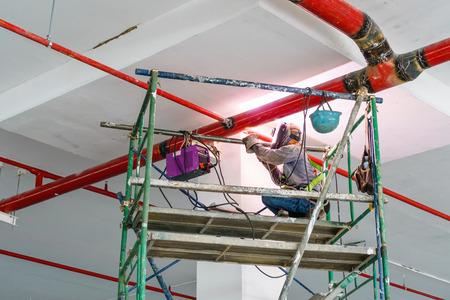 Welder man welding the steel red pipe on the scaffold. An electric welder works on scaffolding.の写真素材