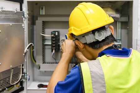 Electrician with a screwdriver macro connect wires on the background of electrical cabinet with relays and terminal blocks.の写真素材