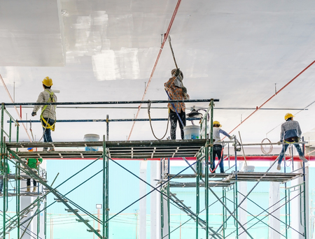 Worker man painting a gypsum plaster ceiling with paint roller on the scaffoldの写真素材