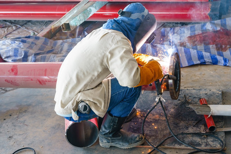 Construction worker welding red steel pipe for fire alarm system in new construction industry.