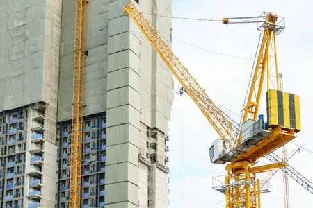 Construction site. Big industrial tower cranes with unfinished high raised buildings and blue sky in...