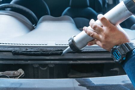 Automobile glazier adding glue on windscreen or windshield of a car in auto service station garage...