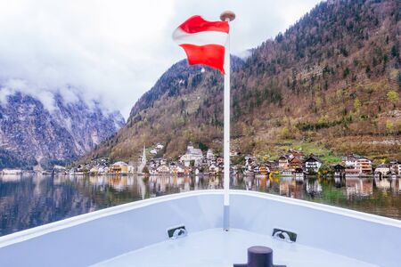 Hallstatt Scenic picture-postcard view of famous mountain village by Lake Hallstatt from Approach Ferry boat with Austrian Flag in the Austrian Alps under Golden Dramatic Sky Sunset in Summer, Austriaの写真素材