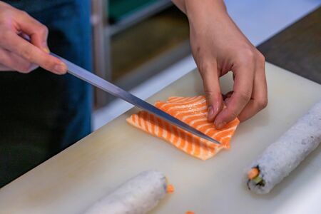 Cutting the salmon with a knife, Japanese chef making sashimi in kitchen, Sushi are madeの写真素材