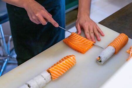 Cutting the salmon with a knife, Japanese chef making sashimi in kitchen, Sushi are madeの写真素材