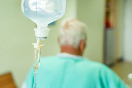 Asian patient older man lying at hospital bed with saline drip showing victory sign. Drop of Saline Solution to Help Patient, iv fluid use for intravenous volume. Selective focusの写真素材