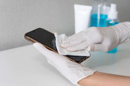 Asian young women cleaning the mobile phone by hand sanitizer gel to eliminate germs, Covid-19, Young woman using alcohol to wipe to avoid contamination, disinfection, outbreak of Coronavirusの写真素材