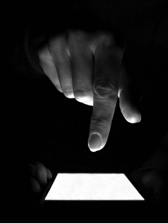Anonymous internet user holds a smartphone in the darkness and finger taps on the screen. Internet crime conceptの写真素材