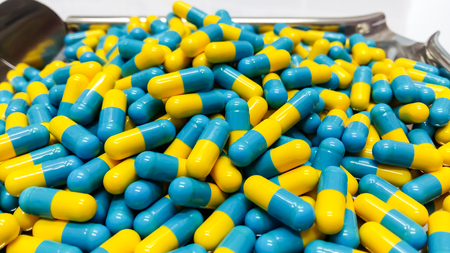 Two tone Medicine Capsules on Stainless Steel drug tray, Yellow Blue Pills and Spatulaの写真素材
