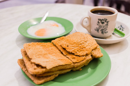 Traditional Singapore Breakfast called Kaya Toast, Coffee bread with Coconut jam and Half-boiled eggs, Oriental Chinese coffee in vintage mug and Original bread toast with kaya a local jam made from eggs, sugar and coconut milk. The fractal on the cup is の写真素材