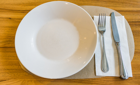 Empty white plate with spoon and knife on wooden background, Concept waiting for foodsの写真素材