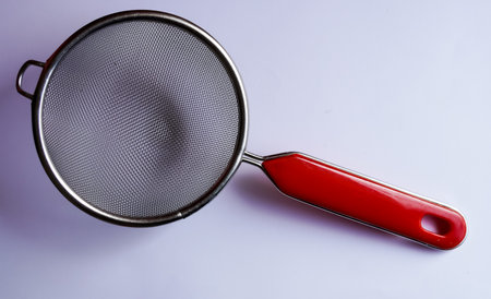Stainless steel sieve with red handle on white background.の写真素材