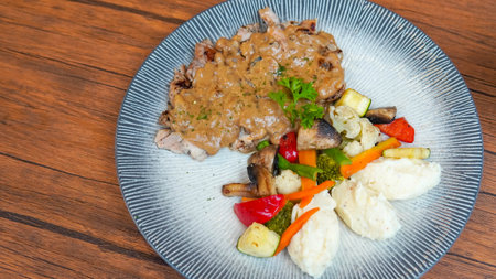 Beef steak with vegetables in a plate on a wooden table.の写真素材