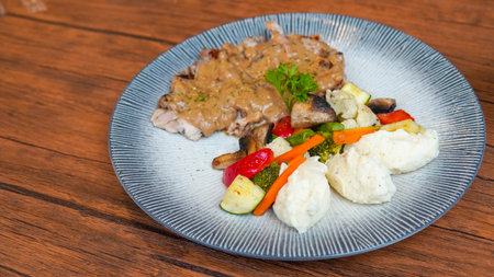 Steak with mashed potatoes and vegetables in a plate on a wooden tableの写真素材