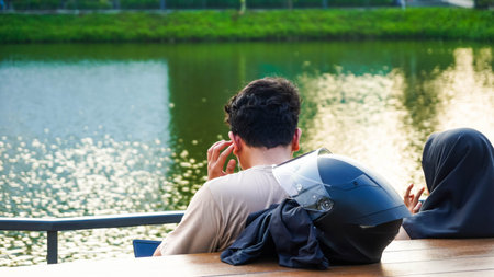 Back view of a man wearing a motorcycle helmet sitting on a wooden bench in a park.の写真素材