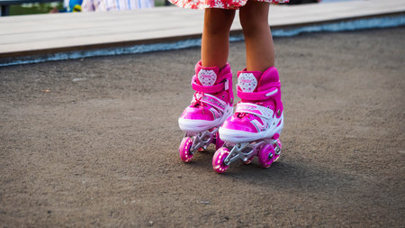 Little girl in pink roller skates on the playground at summer day