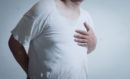 A person in a white shirt clutches their chest, visibly in pain and discomfort. This image symbolizes heart issues, stress, and the urgency of seeking medical attention for health concerns.の写真素材