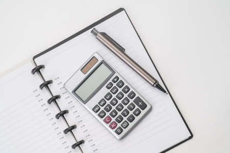 Top view of white table with notebook, calculator and penの写真素材