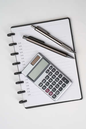 Top view of white table with notebook, calculator and penの写真素材