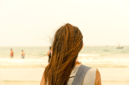 The traveler stand on the sand beach and look people are swimming, The backside head of traveler stand on the sand beachの写真素材