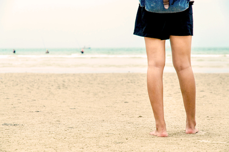 The traveler stand on the sand beach and look people are swimming, The leg of traveler stand on the sand beachの写真素材