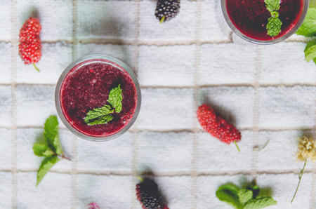 Close-up of mulberry juice and mulberry fruit, Fresh berry fruit and berry smoothies with mint on white fabric.の写真素材