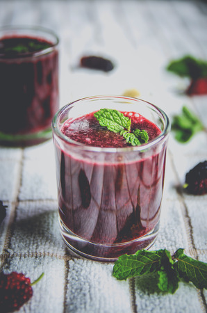 Close-up of mulberry juice and mulberry fruit, Fresh berry fruit and berry smoothies with mint on white fabric.の写真素材