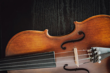 The violin on the dark table, Close - up of violin on the wooden floor, Top view of violin musical on dark wooden floor, Vintage and classic musical instrument used in the orchestra.の写真素材
