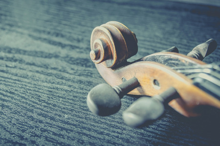 The violin on the dark table, Close - up of violin on the wooden floor, Top view of violin musical on dark wooden floor, Vintage and classic musical instrument used in the orchestra.の写真素材