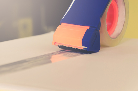 Close - up of parcel box with scissors and scotch tape cutter, Preparing a parcel or package for shipping and delivery, Delivery concept and shipping of parcel.の写真素材