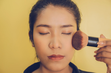 Beauty face of Asian woman by applying brushes, The girl is makeup her face with brush on, Soft and smooth face skin by cosmetics and foundation and using makeup brush on the face.の写真素材