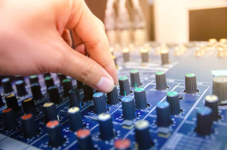 Audio mixer console and professional sound mixing. A hand is adjusting audio mixer with buttons and...