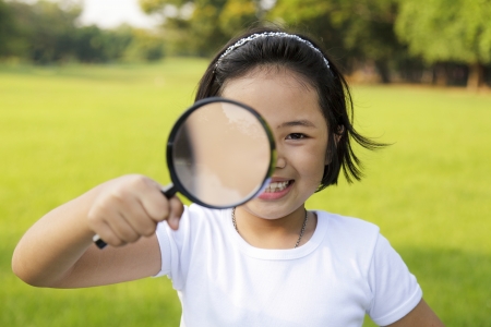 Asian little girl holding a magnifying glass in outdoorの写真素材